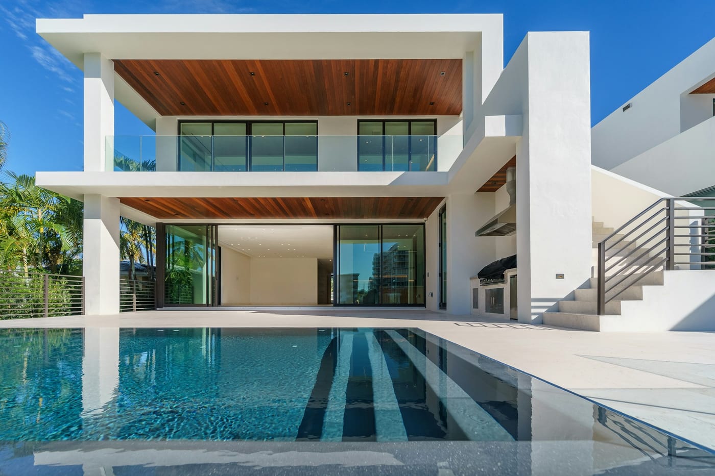 Modern South Florida home with pool, palm trees, and maintained grounds at midday